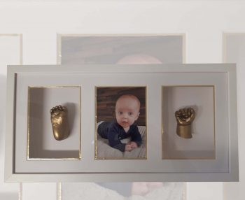 Verdiepte lijst met een babyfoto tussen twee vergulde afgietsels van een handje en een voetje