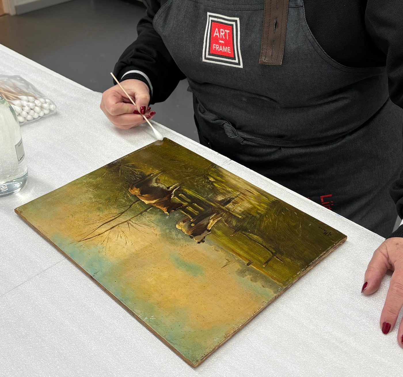 Een olieverfschilderij wordt in het atelier met een wattenstaafje gereinigd, met oplosmiddel en watten binnen handbereik