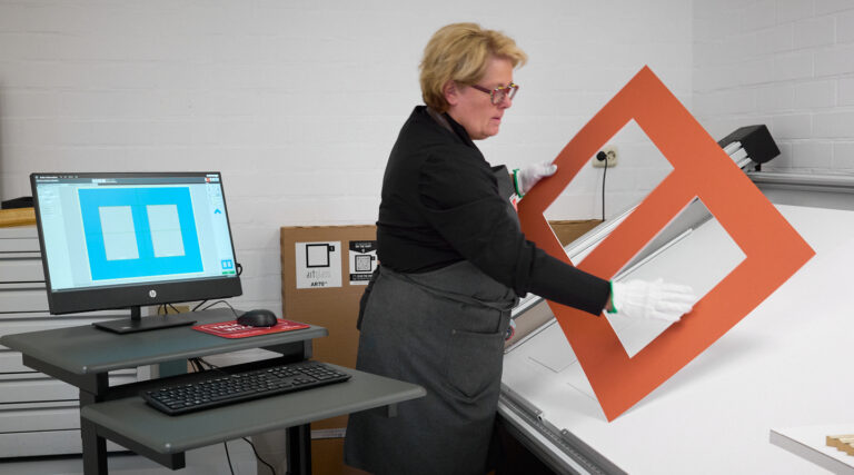 Natascha snijdt een oranje passe-partout op maat aan de computergestuurde snijtafel